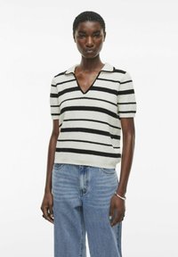 Polo de punto a rayas con rayas horizontales en blanco y negro, mangas cortas y un cuello en V. Combinado con unos vaqueros de mezclilla azul claro.