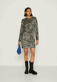 Μαύρο και ασημί φόρεμα με πούλιες, μακρύ μανίκι, στρογγυλή λαιμόκοψη και εφαρμοστή σιλουέτα. Συνδυασμένο με χοντρά μαύρα μποτάκια και μπλε τσάντα.