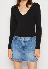 Svart långärmad bodysuit med V-ringning, parat med en ljusblå denimminikjol med sidofickor och knappstängning framtill.