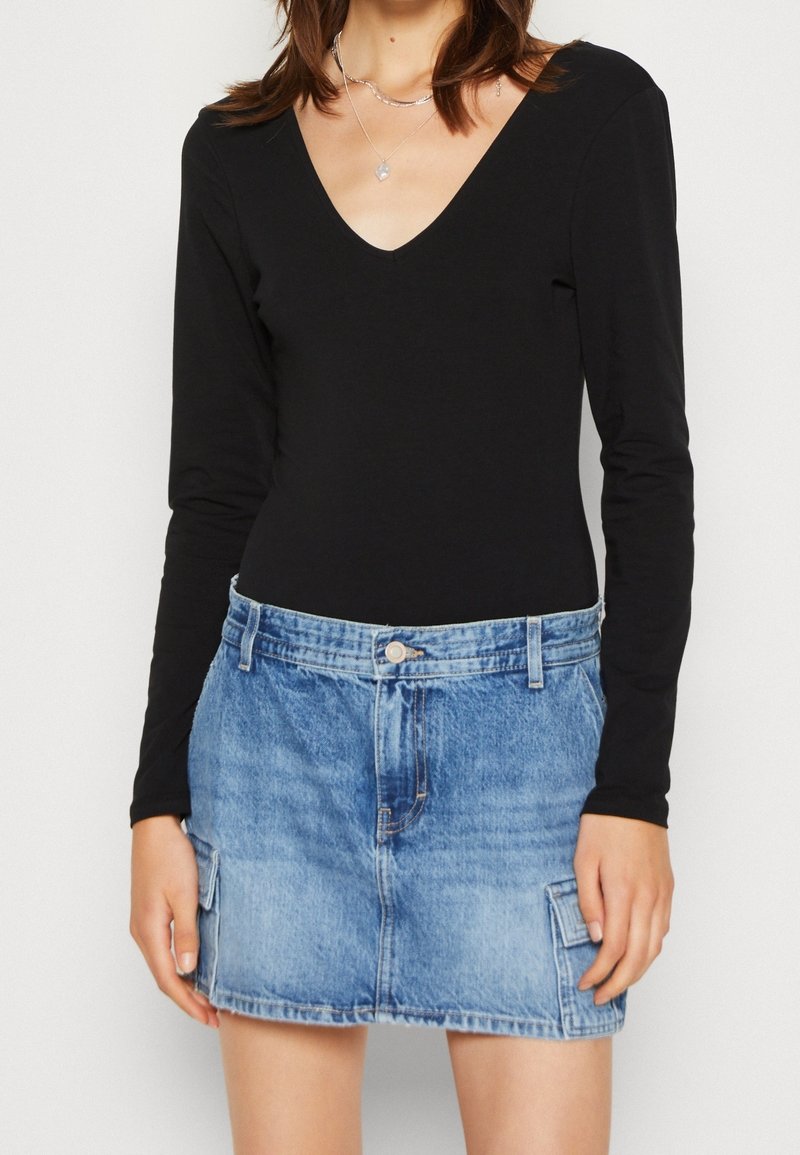 Svart långärmad bodysuit med V-ringning, parat med en ljusblå denimminikjol med sidofickor och knappstängning framtill.