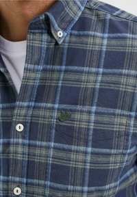 Kostkovaná flanelová košile v námořnické modři a zelené, s bílými knoflíky, límečkem na knoflíky a malým zeleným vyšívaným logem na hrudi.