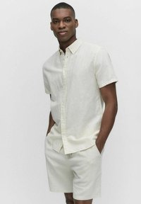 Korte mouwen, geknoopte blouse en shorts set in lichtbeige linnen. Kenmerken zijn knoopsluiting, ontspannen pasvorm en een zachte textuur.