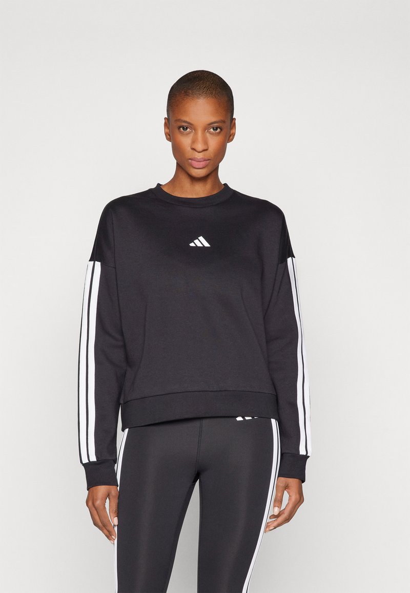 Črna trenerka s belim Adidas logotipom, dolgi rokavi s belimi črtami ob straneh in oblikovan rez na robu.