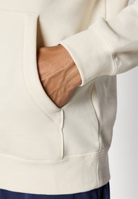 Sweatshirt beige clair avec une poche kangourou et des poignets côtelés. Tissu doux et texturé avec une coupe décontractée.