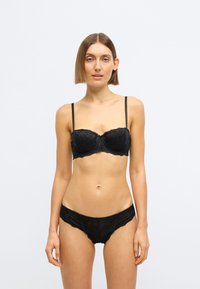 Čierna čipkovaná podprsenka a zodpovedajúce nohavičky s kvetinovými vzormi, tenkými ramienkami a vlnitým lemom, ktoré ukazujú priehľadné textúry a priliehavý strih.