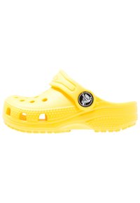 Sabot en mousse jaune avec un design de trou de ventilation, sangle de talon ajustable et accent logo circulaire sur le côté. Semelle texturée.