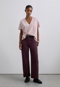 Jasnoróżowy t-shirt z dekoltem w serek, zestawiony z szerokimi bordowymi spodniami, ozdobionymi czarnym paskiem i czarnymi mokasynami, o gładkiej fakturze materiału.