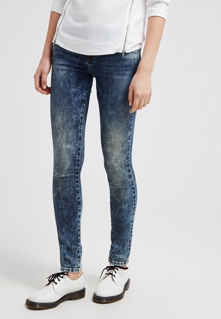 Jean skinny en denim bleu délavé, avec des effets d'usure légers. Associé à un haut blanc à manches longues et des chaussures noires à lacets.