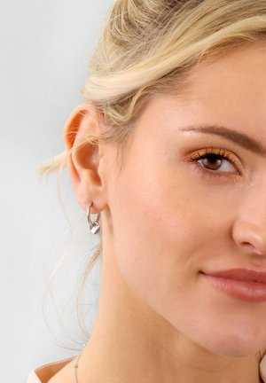 Silver hoop earrings with a small, decorative element. Sleek, polished surface with a smooth texture, displaying modern and minimalist design.