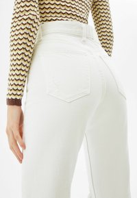 White high-waisted jeans with a straight-leg cut, featuring a rear pocket design and a slight distressed detail on the fabric texture.