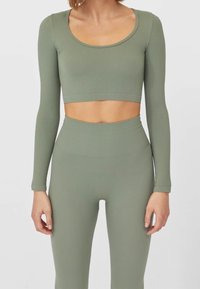 Olive green ribbed matching crop top and high-waisted leggings. The top features long sleeves and a scoop neckline. Soft texture.