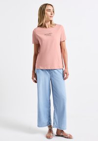 T-shirt en coton rose à manches courtes et col incurvé, avec un imprimé en écriture noire. Associé à un jean à jambes larges bleu clair.