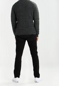 Svarta jeans som matchas med en strukturerad, mörkgrå stickad tröja med ribbade detaljer på axlarna och en figursydd design. Vita sneakers fulländar looken.