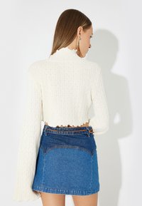 Krämfärgad ribbad långärmad topp med vågig halsringning, tillsammans med en blå denim mini kjol med färgblockdesign och läderbälte.