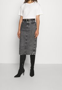 Černá denimová midi sukně s předními kapsami a předním švem, v kombinaci s bílým tričkem a černými vysokými semišovými botami až po kolena.