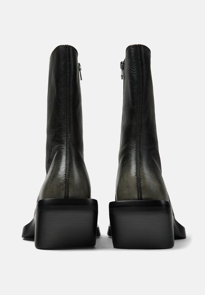 Paar schwarze Leder-Stiefeletten mit quadratischen Absätzen, Rückansicht vor einem weißen Hintergrund.