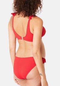 Ensemble de bikini rouge à côtes avec un haut de soutien-gorge ajusté doté de bretelles volantées et d'un dos à fermeture, associé à un bas taille mi-haute. Texture lisse et couleur vive.