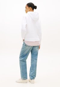 Biała bluza z kapturem, luźny krój, z prążkowanym wykończeniem na dole. Jasnoniebieskie dżinsy o prostych nogawkach, noszone nieco luźno. Białe trampki.