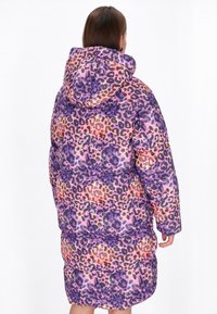 Pūkains garsais mētelis purpura, oranžā un rozā leopardu rakstā; aprīkots ar kapuci un quilted tekstūru siltumam.