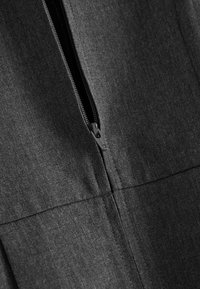 Close-up of a partially unzipped black zipper on dark gray textured fabric, showing seam details and zipper pull.