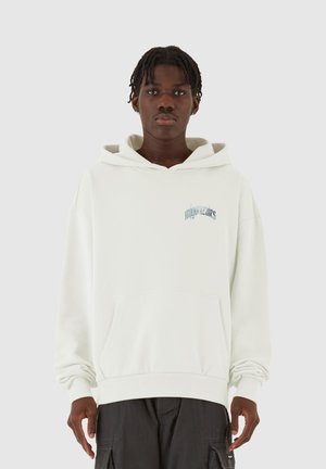 Lysbeige oversized hoodie med en frontlomme, snøre i hætten og diskret blå tekst på brystet. Blødt stof, afslappet pasform.