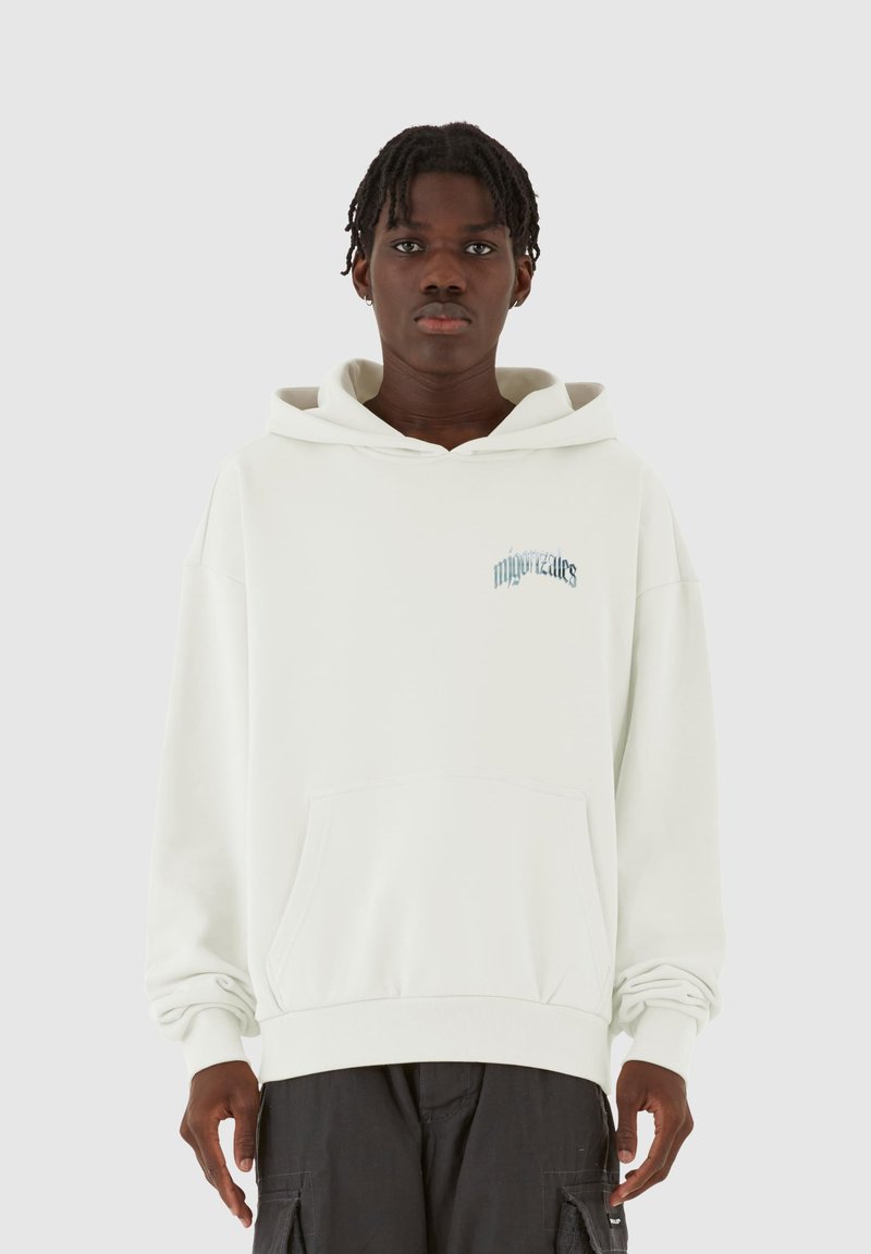 Sudadera oversized de color beige claro con un bolsillo frontal, capucha con cordón y texto azul sutil en el pecho. Tejido suave, corte relajado.