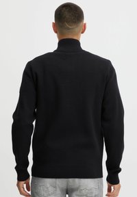 Svart genser med høy hals, ribbestrikkede mansjetter og nederkant, laget av et glatt, strikket materiale. Enkel design, ingen synlige mønstre eller logoer.
