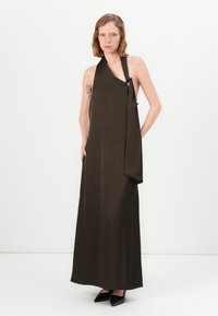 Lång, mörkbrun halterneck klänning i mjukt tyg, med en asymmetrisk design som har ett draperat överlägg och en diskret axelknäppning.