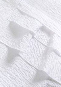 Nærbillede af krøllet hvidt stof med en foldet manchet, der har synlige sømme og subtile skygger.