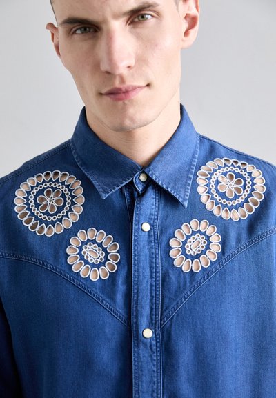 Dunkelblaue Jeanshemd mit gestickten Blumenmotiven. Verfügt über Ausschnittdetails, einen spitzen Kragen und Druckknöpfe entlang der Vorderseite.