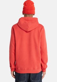 Sudadera roja con un corte holgado, que presenta una capucha amplia y puños de canalé. Combinada con un gorro a juego, ambos hechos de un tejido suave.