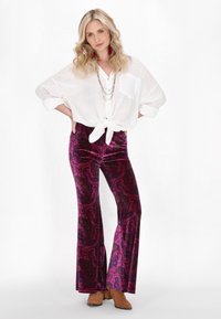 Hvid, løstsiddende blouse med bundet front og to brystlommer, parret med lilla paisley-mønstrede flared bukser i velour og brune ankelstøvler.