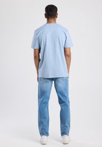 Light blue short-sleeve T-shirt made of cotton, worn with light blue jeans and white sneakers. Simple design with a round neckline.