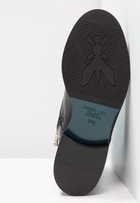 Černé kožené kotníkové boty s texturovanou gumovou podešví, na které je zobrazen vzor loga a embosované detaily značky, velikost 37,5.