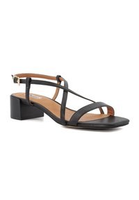 Sandale en cuir noir avec un petit talon carré. Présente plusieurs fines lanières, un design à bout ouvert et une sangle de cheville avec un détail de boucle dorée.