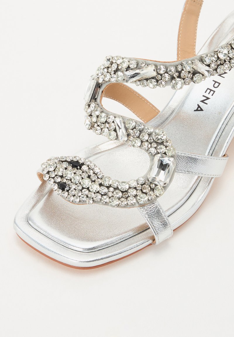 Sandale à talons hauts en argent avec un orteil carré, décorée de plusieurs strass transparents et noirs dans un design serpent sur la lanière.