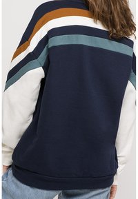 Felpa navy con strisce bianche, teal e ruggine. Progettata con una vestibilità rilassata, orlo a costine e una texture morbida. Mostrata vista posteriore.