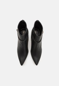 Botas de tobillo de cuero negro con un diseño de punta afilada, que cuentan con una textura suave y un cierre lateral con cremallera.