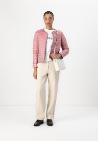 Casaco acolchoado rosa claro com um design justo, usado sobre um sweatshirt branco com gráfico; combinado com calças largas beiges e sapatos pretos.