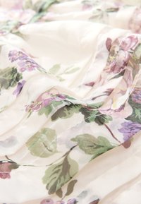 Prosojni cvetlični material z vijoličnimi in zelenimi vzorci na belo-belem ozadju, z nežnimi gubami in mehko teksturo.
