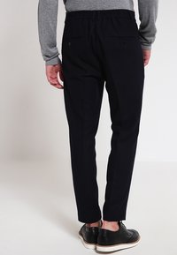 Tmavě modré kalhoty s úzkým střihem, elastickým pasem a dvěma zadními kapsami, doplněné černými botami a šedým dlouhým rukávem.