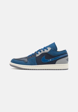 Baskets basses avec des panneaux bleus, bleu marine et gris, lacets bleus, semelle blanche et un swoosh Nike bleu sur le côté.