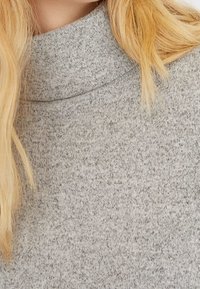 Grau, weicher Rollkragenpullover aus gestricktem Stoff mit dezentem strukturiertem Muster und lockerer Passform. Nahaufnahme des Halsausschnitts und der Textur.