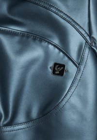 Tessuto in ecopelle blu con finitura lucida, caratterizzato da cuciture curve e un piccolo emblema nero cucito sulla superficie.