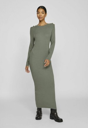 Knit dress in olive green, long-sleeved, ribbed texture, featuring button accents on shoulders, paired with black ankle boots.