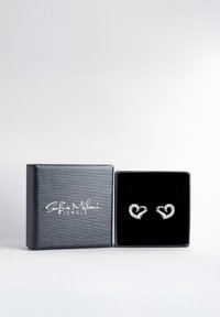 Silver hjärtformade örhängen med gnistrande detaljer, presenterade i en grå texturerad låda med svart inredning. Lådan har varumärkets logotyp.