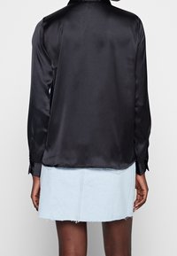 Camicia nera di raso a maniche lunghe con colletto, caratterizzata da una texture liscia e polsini con bottoni, abbinata a una gonna di jeans sbiadita.