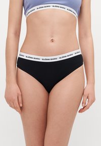 Schwarze Baumwoll-Bikini-Unterhosen mit einem weißen elastischen Bund, auf dem das Logo "BJÖRN BORG" prangt. Enganliegendes Design mit glatter Textur.