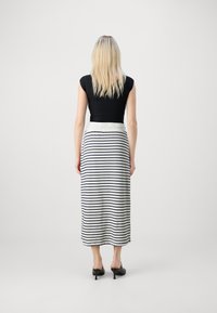 Svart tettsittende topp kombinert med et langt, stripete skjørt i hvitt og marineblått. Skjørtet har en hvit midjebånd og faller under leggen.