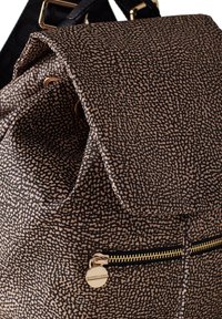 Zaino in tessuto patterned con un design maculato marrone e nero, dotato di una zip dorata e dettagli hardware. Texture morbida con chiusura a pattina.